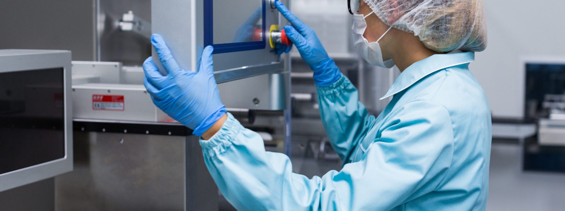 caucasian factory worker in blue lab suit configures machine, look at control panel